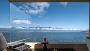 Een moderne kamer met een groot raam met uitzicht op een waterpartij en verre bergen.