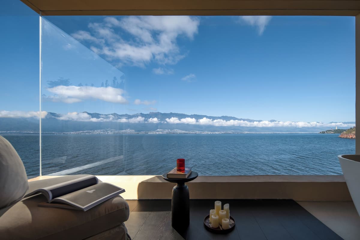 A modern room with a large window overlooking a body of water and distant mountains.