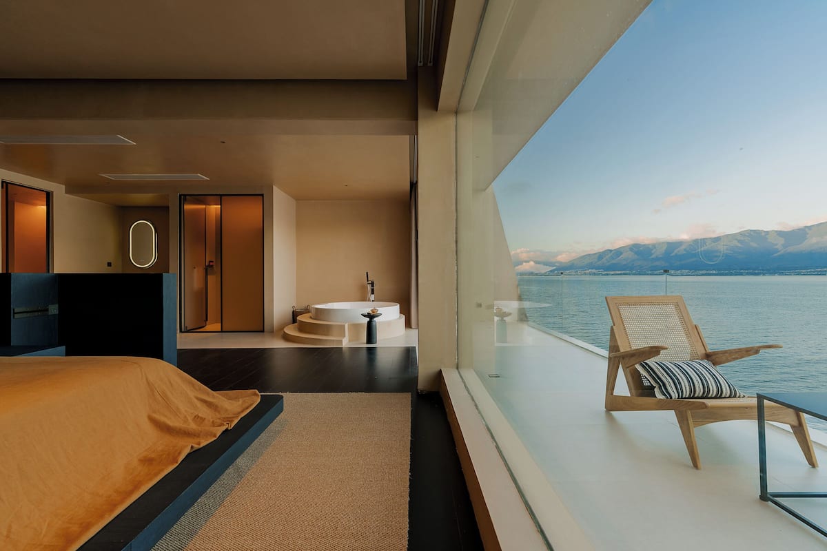 A modern bedroom with a large bed, a circular sink, and a view of the sea.