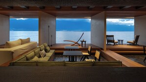 Een modern interieur met een groot raam met uitzicht op water en bergen. Er zijn meerdere zithoeken met banken en stoelen.