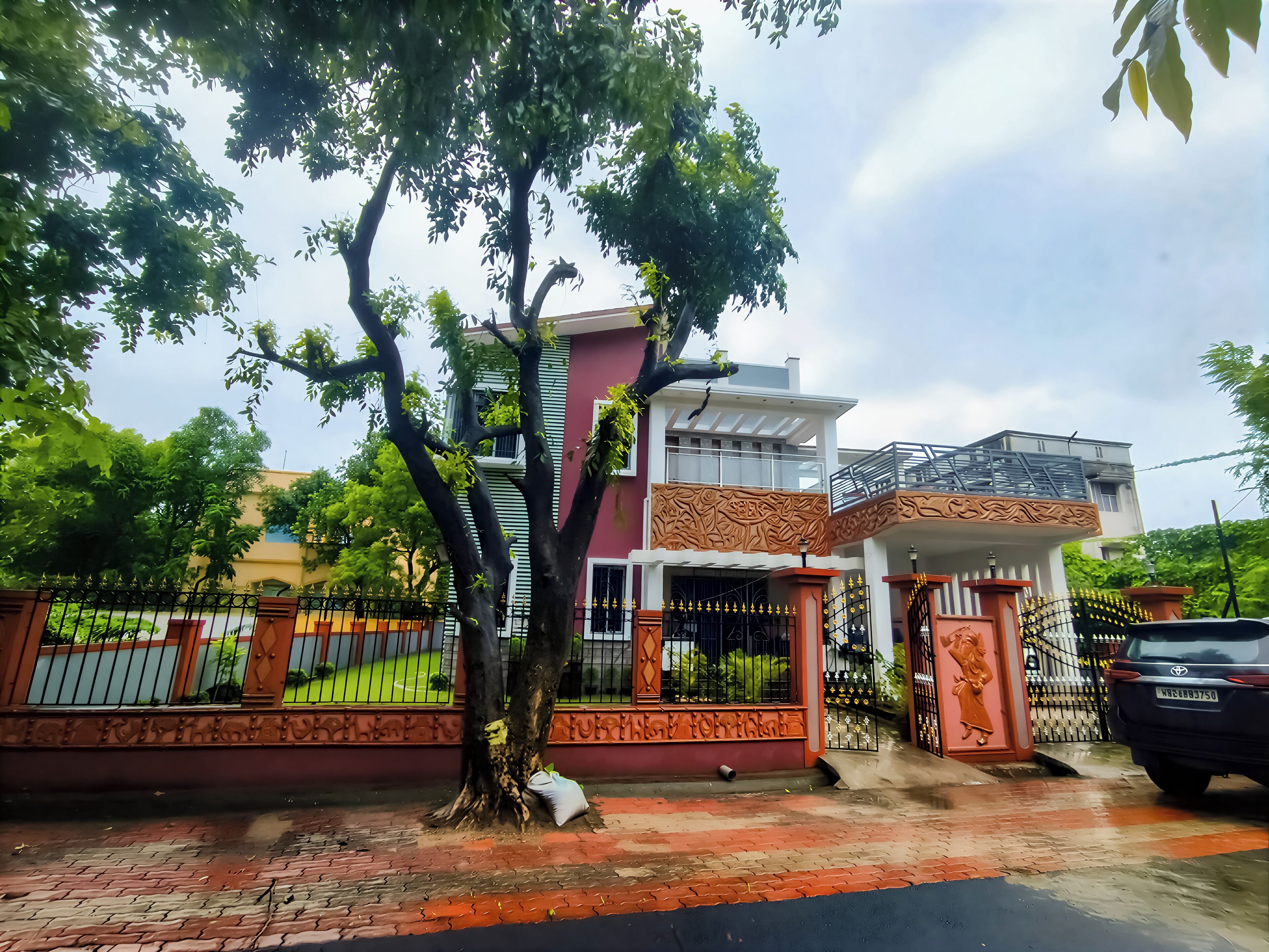 A two-story house with a balcony, a gated entrance, and a tree in front.