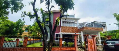 A two-story house with a balcony, a gated entrance, and a tree in front.