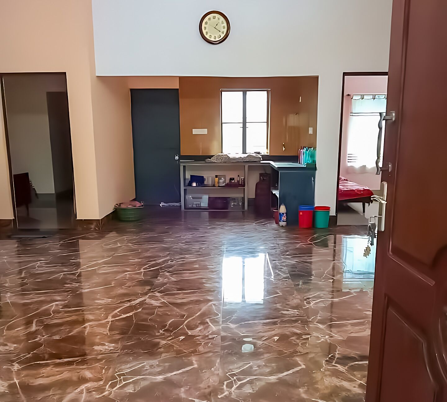 A spacious room with a polished marble floor, a large window, a desk with a chair, and a bed with a red blanket.