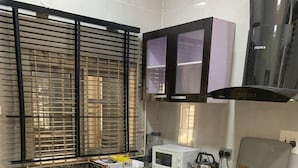 A compact kitchen with a gas stove, microwave, and a refrigerator. - ELLEX SLEEVES APARTMENT  (Ibadan)