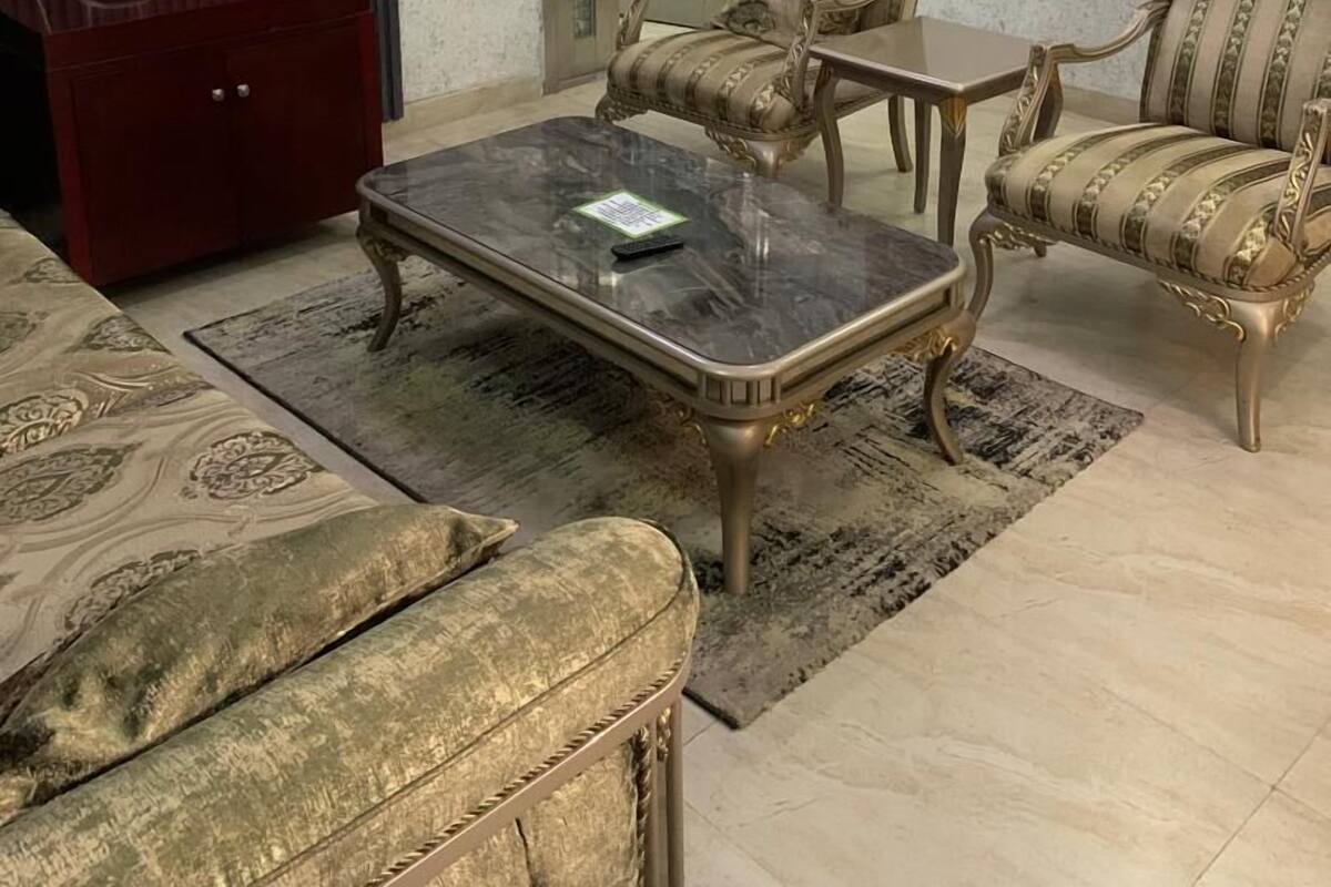 A living room with a television, a red cabinet, a marble coffee table, two armchairs, and a patterned rug.