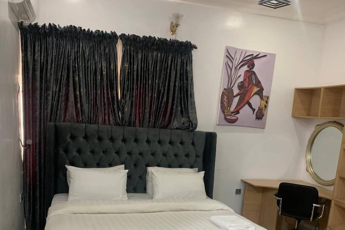 A neatly arranged bedroom with a large bed, a desk, a chair, and a wall-mounted mirror.