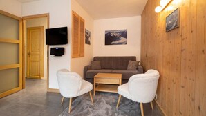 Una sala de estar acogedora con un sofá, dos sillones, una mesa de centro, un televisor de pantalla plana, contraventanas de madera y un cuadro enmarcado en la pared.