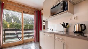 Una cocina moderna con microondas integrado, hervidor y ventana con vistas a un balcón con una silla.