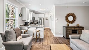 A modern living room with grey sofas, a wooden coffee table, and a kitchen with white cabinets and a stainless steel refrigerator. - 2BR near Gulf Place w/ Pool, Grill + Free Tickets: Dolphin Cruise & More! (Santa Rosa Beach)