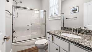 A bathroom with a glass-enclosed shower, a white toilet, a granite countertop sink, and a framed picture on the wall. - 2BR near Gulf Place w/ Pool, Grill + Free Tickets: Dolphin Cruise & More! (Santa Rosa Beach)