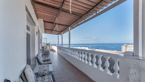 A covered balcony with seating, a view of the sea, and a railing.