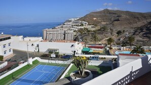 A coastal view with a tennis court, buildings, and a mountain in the background.