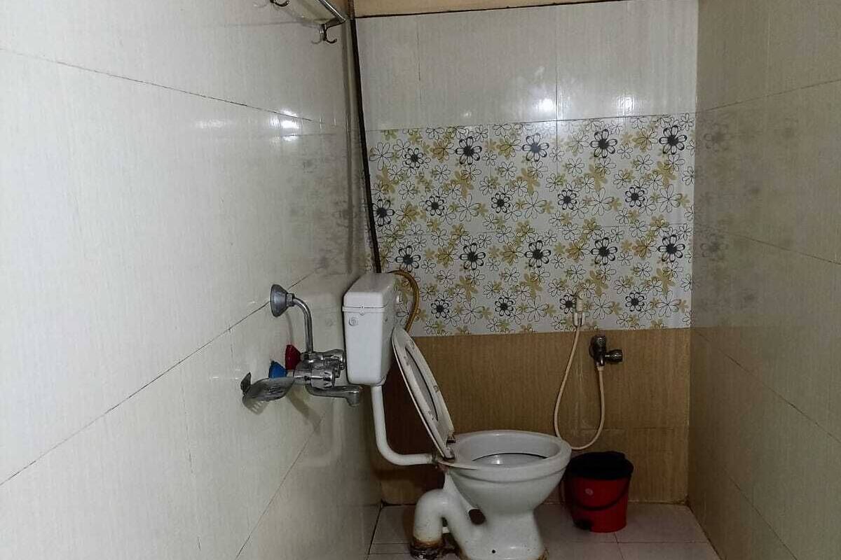 Une petite salle de bain carrelée, équipée de toilettes, d’un seau vert et d’une douche.