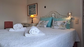 A neatly made bed with white linens and rolled towels, a bedside table with a lamp, and a wall-mounted painting. - Apartment in the city center with spectacular views and easy access. (Ponta Delgada)