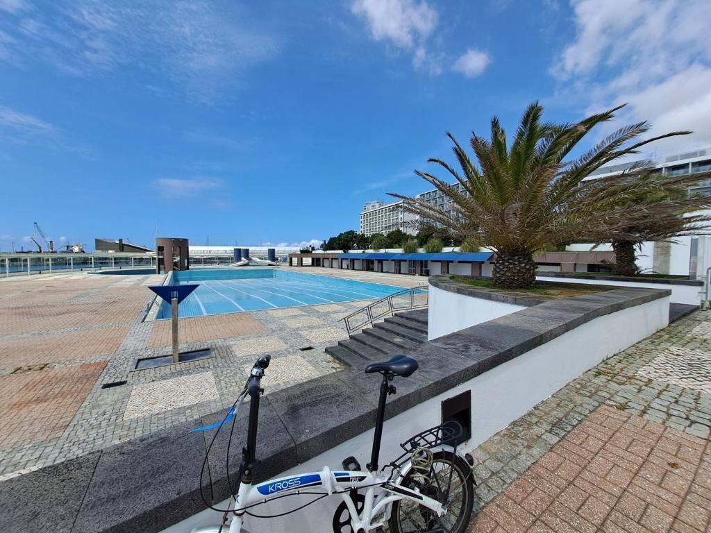 Zona de piscina con una bicicleta, escaleras que llevan a un edificio y una palmera.