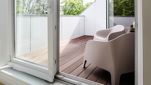 A room with a large sliding glass door leading to an outdoor area with a wooden deck and a white chair. - Louis and Louise Apartments & Lofts  (Bremen)