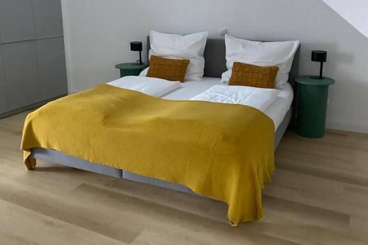 A modern bedroom with a bed, two nightstands, and a green trash bin.
