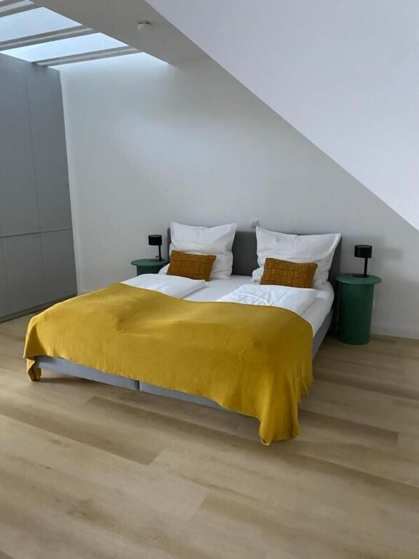 Une chambre moderne avec un lit, deux tables de chevet et une poubelle verte.