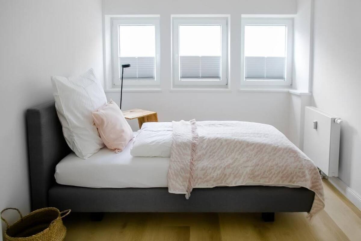 A bedroom with a bed, a bedside table, a lamp, and three windows.