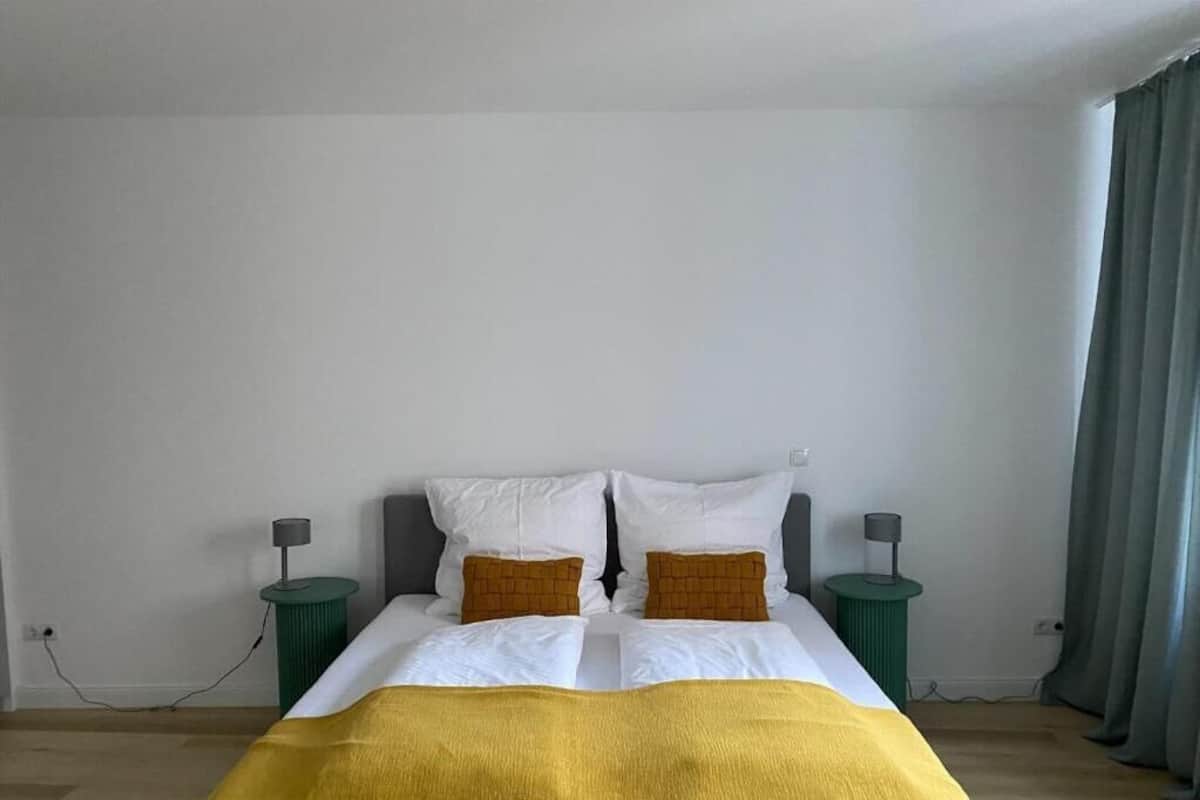 A bed with a yellow blanket, white pillows, and two green nightstands with lamps.