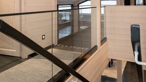 A modern interior with a wooden staircase, glass railings, and pendant lighting.