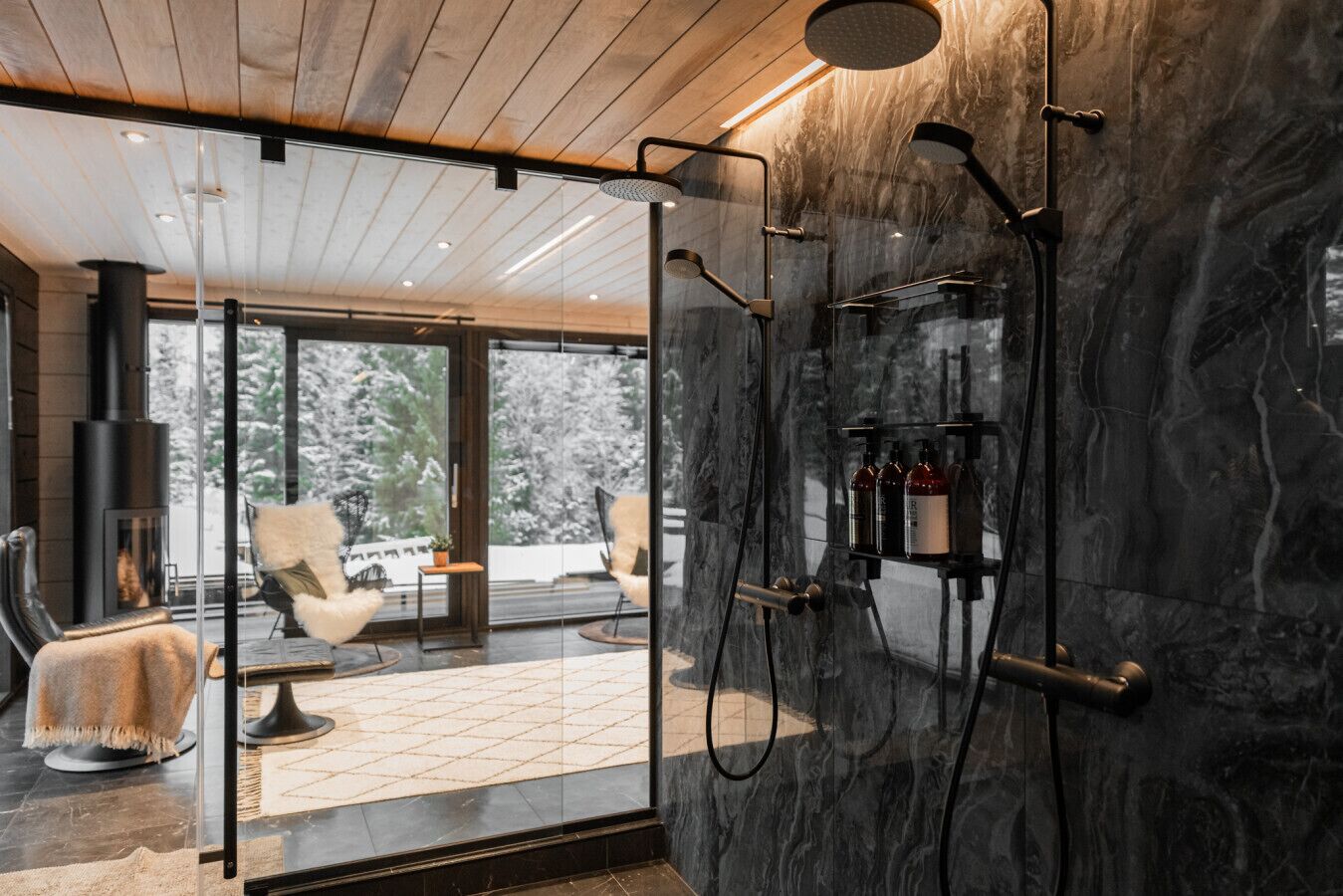 A modern bathroom with a glass shower enclosure, a marble wall, and a visible fireplace in the adjacent room.