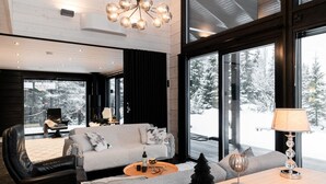 A modern living room with a sofa, coffee table, and a lamp. There is a view of a snowy landscape through large windows.