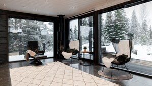 A modern interior with large windows, a fireplace, and three black chairs with white fur throws.
