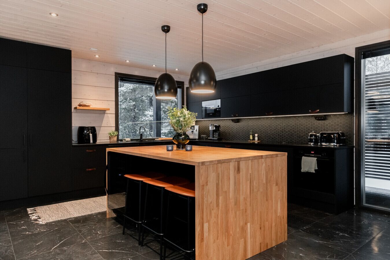 Een moderne keuken met een centraal eiland, zwarte kasten en hanglampen.
