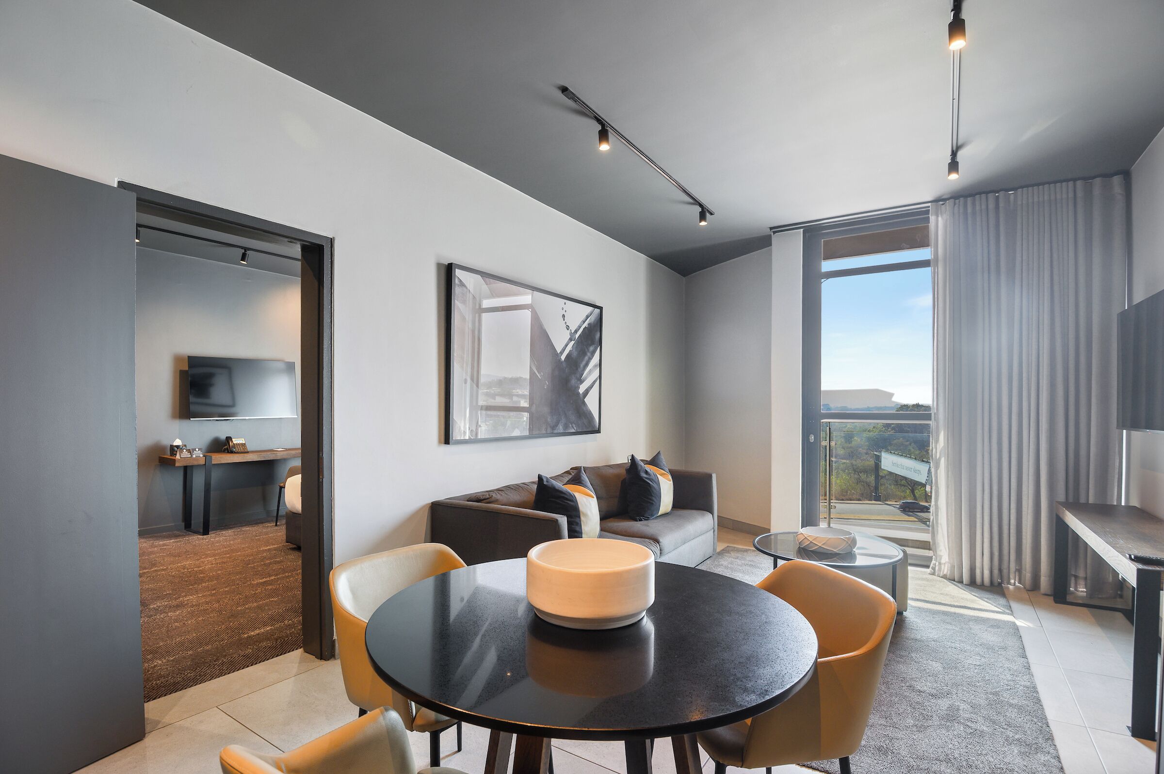 Une chambre d’hôtel moderne dotée d’une grande fenêtre, d’un canapé, d’une table à manger et d’un téléviseur.