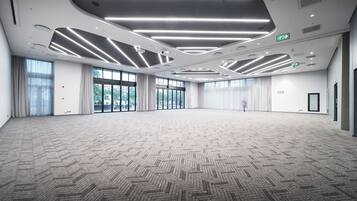 Una sala de conferencias amplia, bien iluminada, con un diseño moderno en el techo, ventanas grandes y una alfombra estampada.