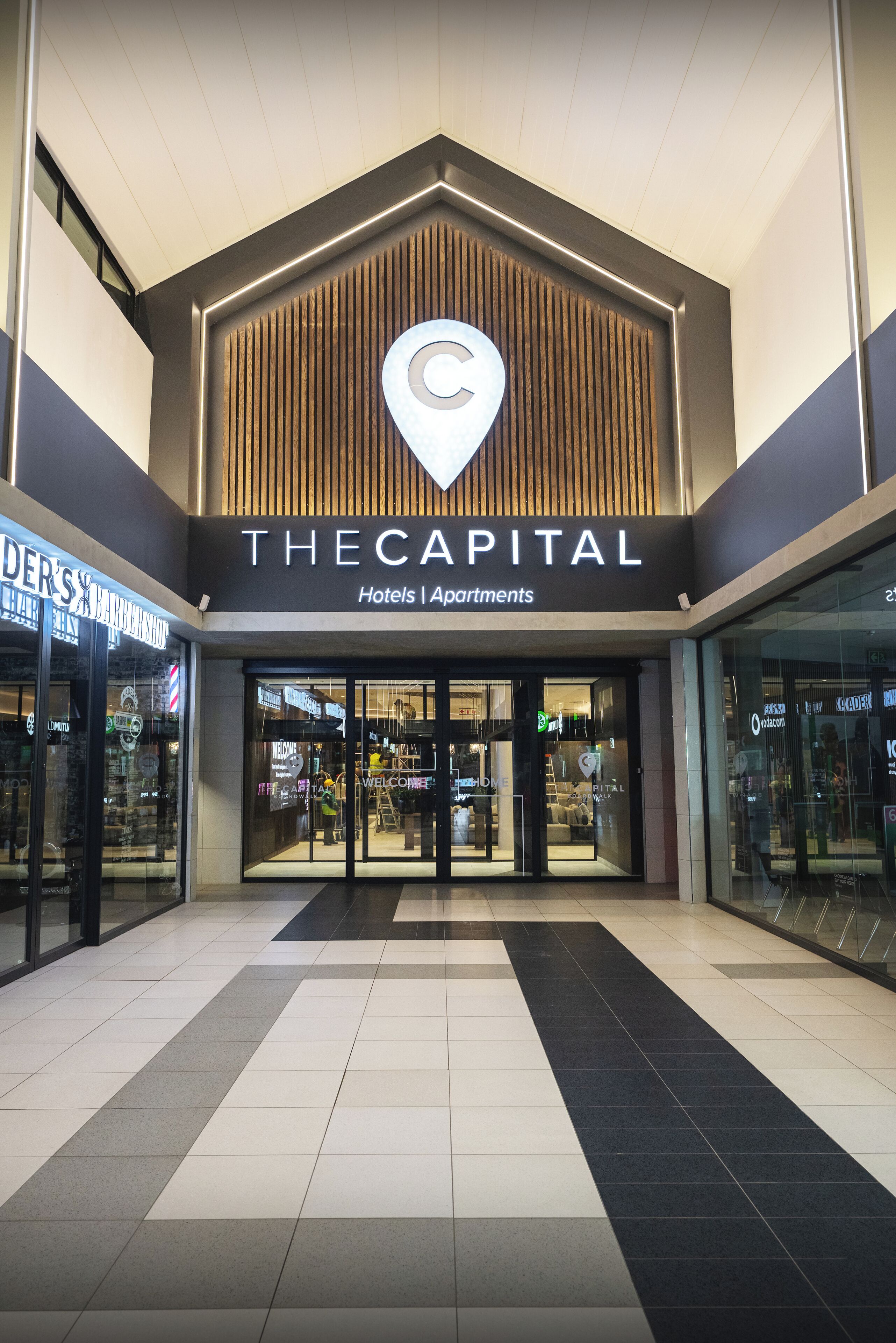 A hotel entrance with a prominent logo, a sign indicating it's a hotel and apartments, and a modern design with a tiled floor.