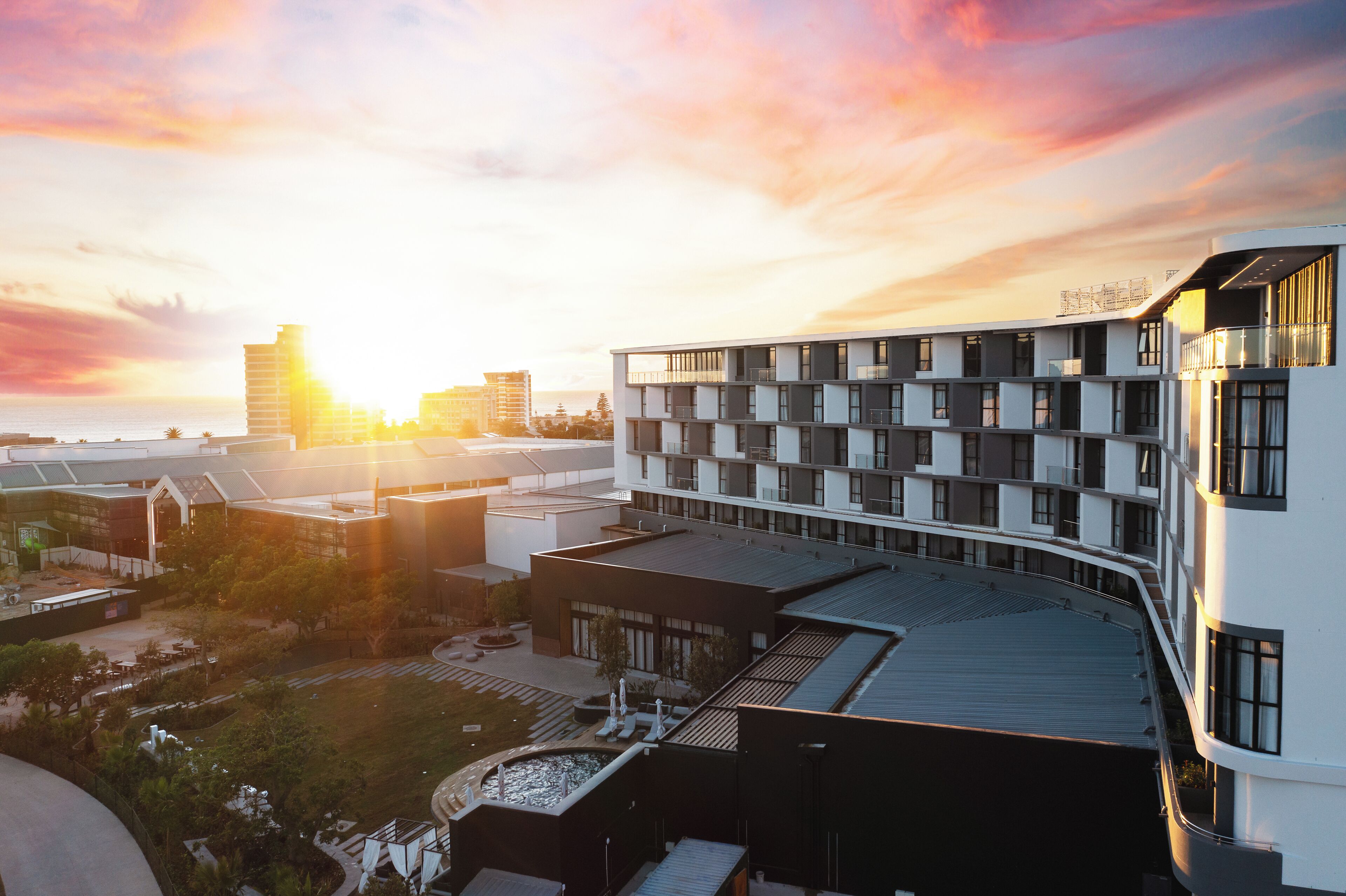 A modern hotel with a rooftop terrace, multiple floors, and a view of the sunset.