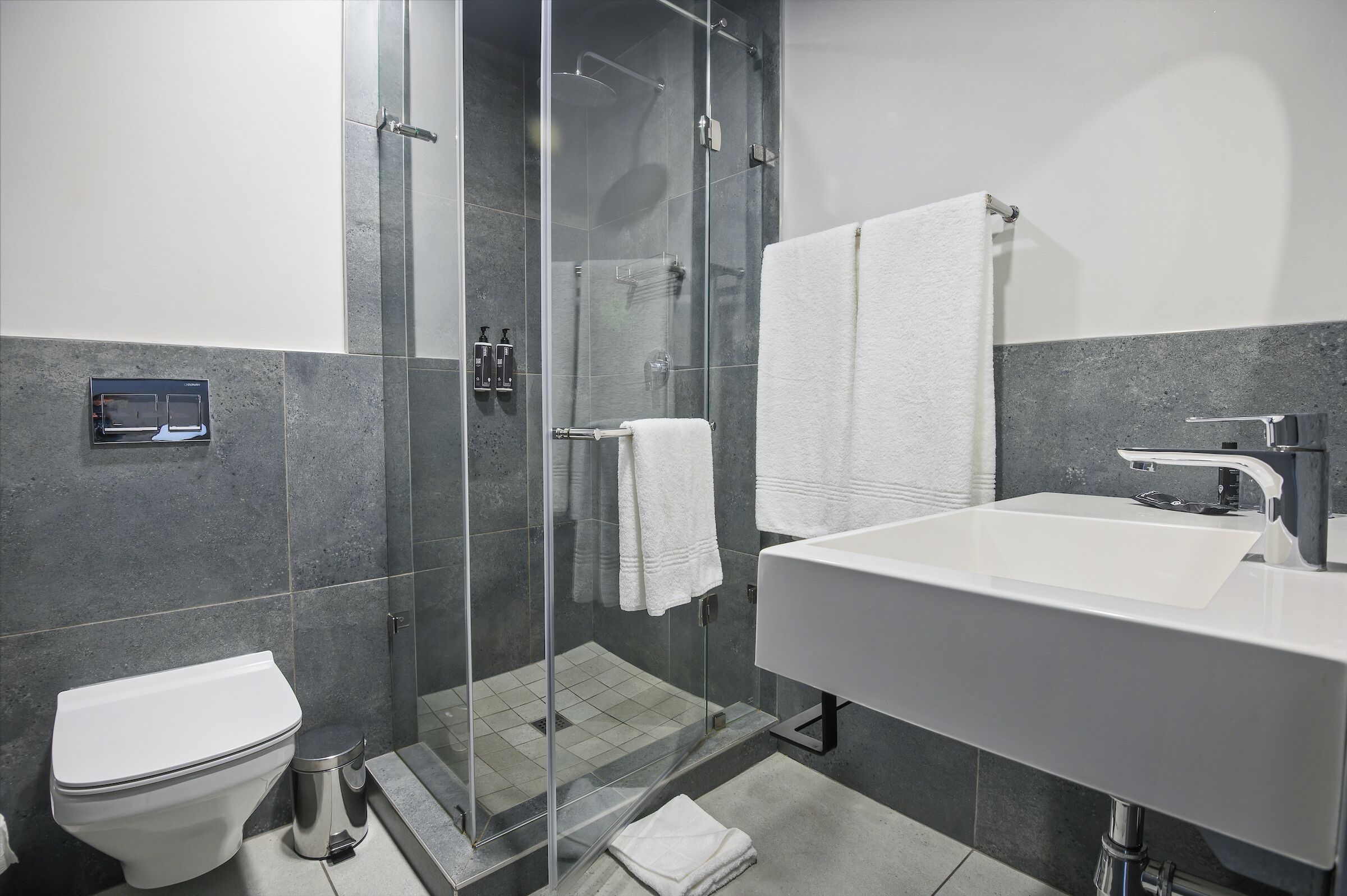 A modern bathroom with a glass-enclosed shower, a white sink, and a toilet.