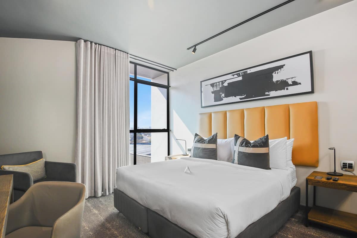Una habitación de hotel con una cama grande, una silla, una mesita de noche y una ventana con cortinas.