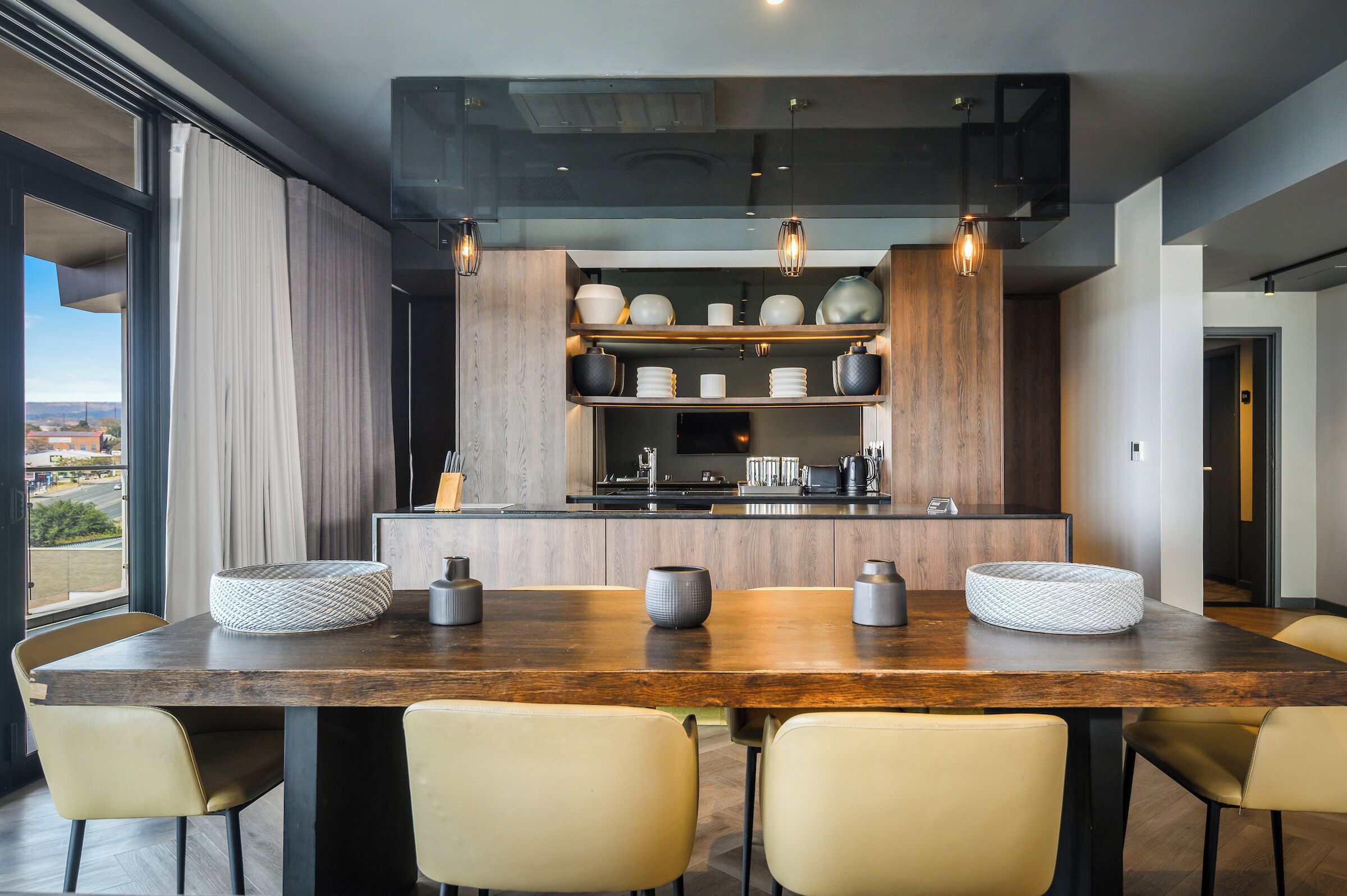 Une cuisine moderne dotée d’un îlot central en bois, d’étagères intégrées et de luminaires suspendus.