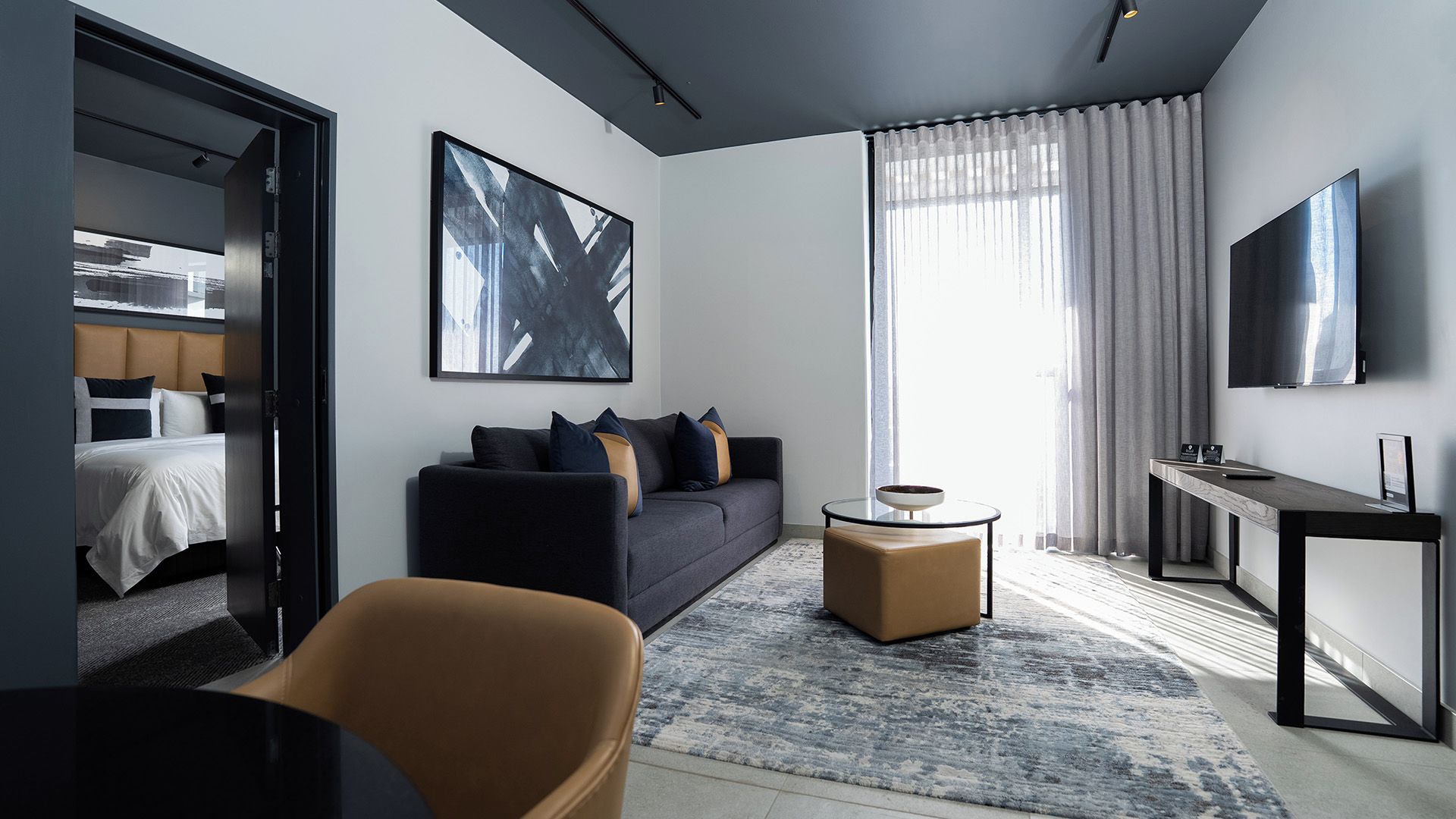 A modern hotel room with a bed, a sofa, a coffee table, and a TV.