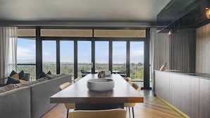 A modern dining area with a large table, cushioned seating, and a view of the outdoors. - The Capital Boardwalk (Gqeberha)