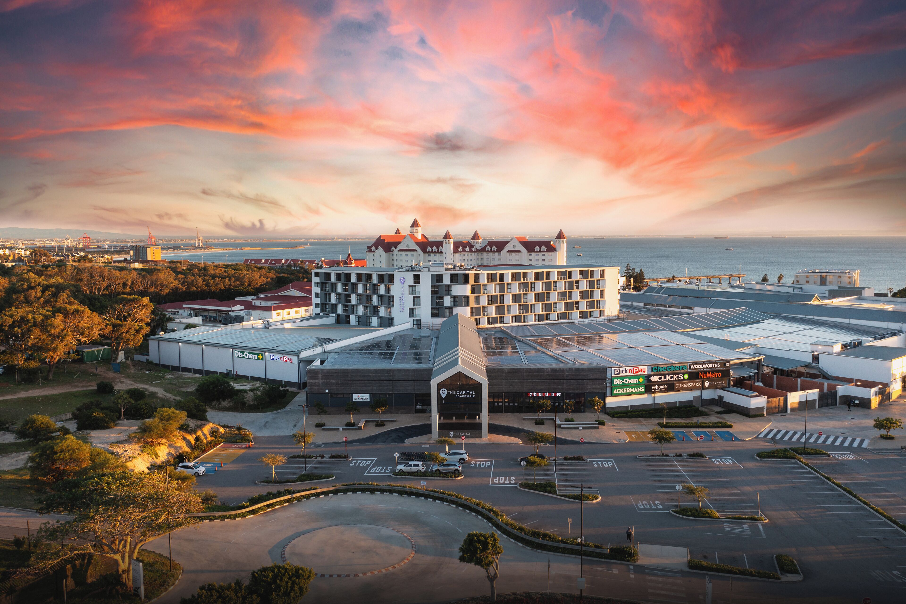 A large hotel with a central courtyard, multiple parking lots, and a view of the sea.