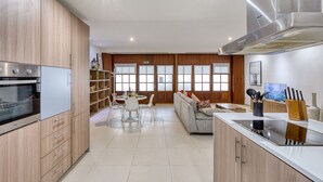 A modern kitchen with wooden cabinets, a built-in oven, and a dining area with a white table and chairs. - Spacious waterfront 1-bedroom apartment GSPI1-1 (Birgu)