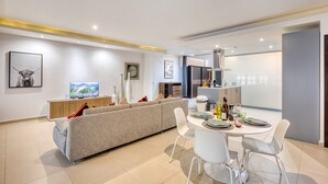 A modern living room with a sofa, a TV, and a dining area with chairs and a table. - Spacious waterfront 1-bedroom apartment GSPI1-1 (Birgu)