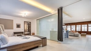 A modern hotel room with a large bed, a glass partition, a sofa, and a small table. - Spacious waterfront 1-bedroom apartment GSPI1-1 (Birgu)