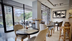 A modern dining area with round tables and chairs, large windows, and a decorative wall with horse silhouettes. - Le Basilic Addis Hotel Apartment & Spa (Addis Ababa)