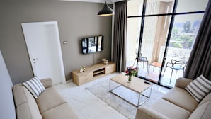 A modern living room with a sofa set, a coffee table, a TV, and a balcony with outdoor seating. - Le Basilic Addis Hotel Apartment & Spa (Addis Ababa)