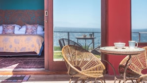 A bedroom with a bed, a ceiling fan, and a view of the sea through a large window. - Boho Ocean-View Villa: Pool & Walk to Beach (Murdock Valley)