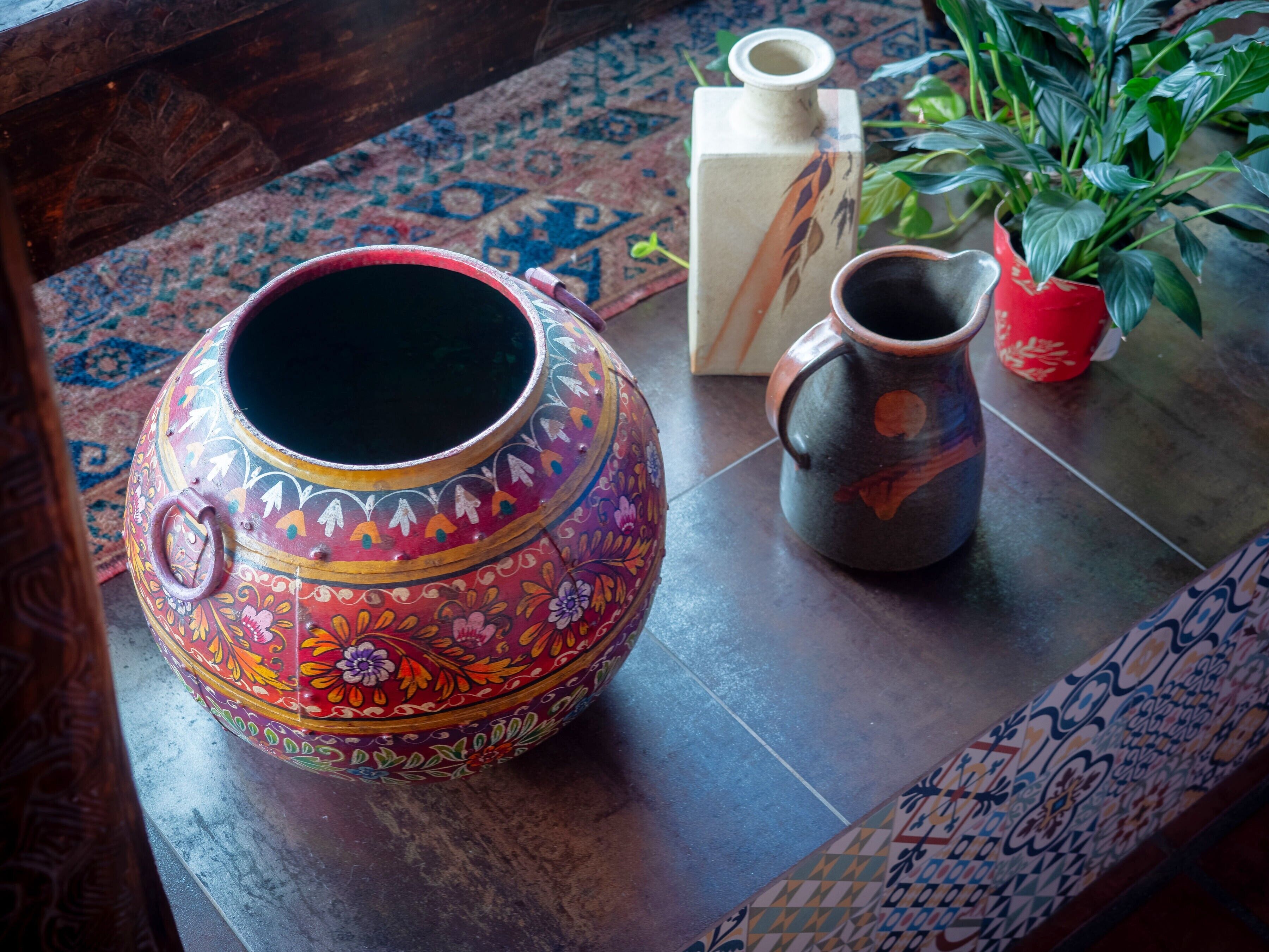 Une table ornée d’un grand pot en céramique décorative, d’un pichet en céramique plus petit et d’une plante en pot.