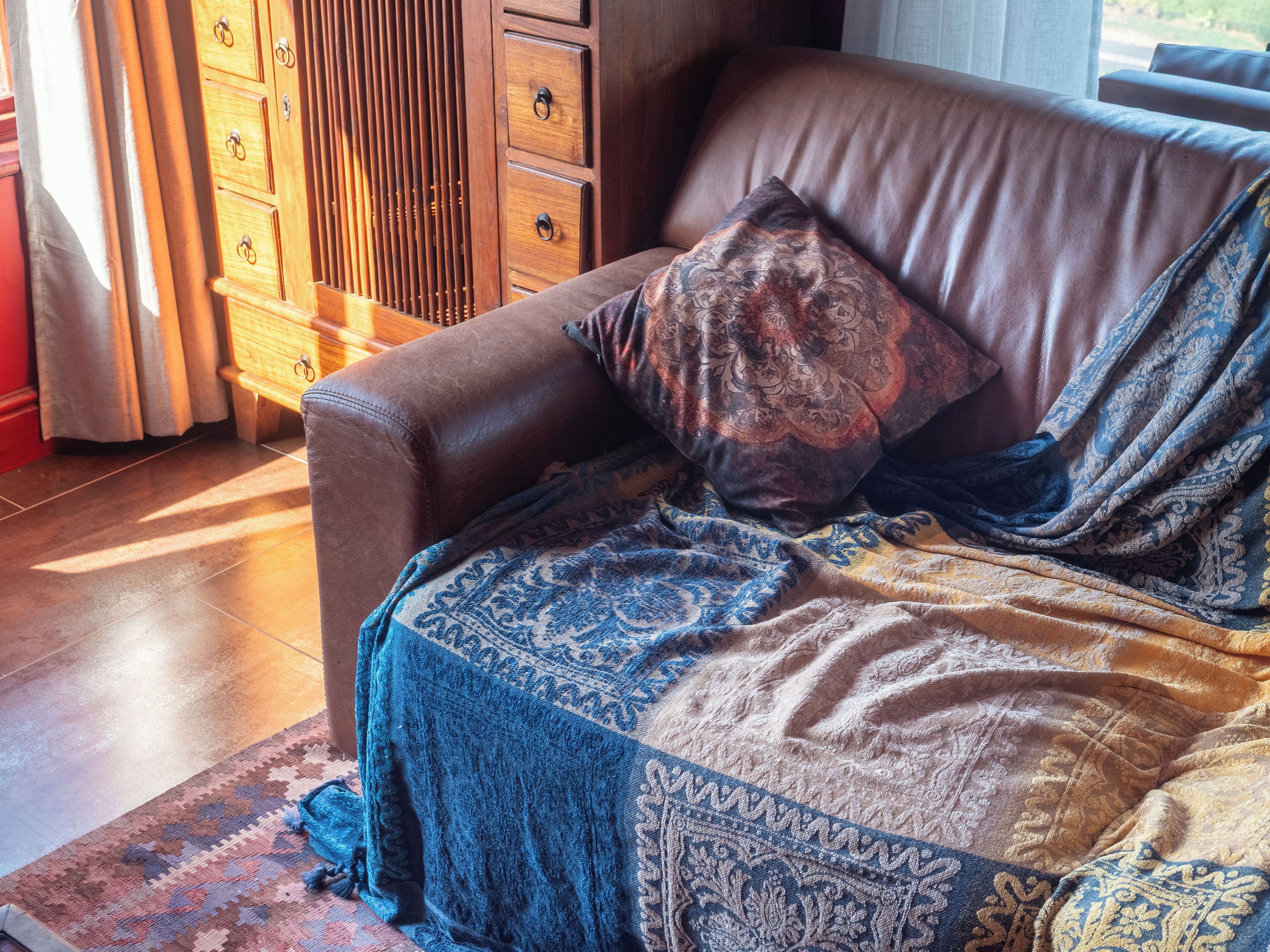 A brown leather sofa with a patterned throw blanket and a decorative pillow.