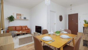 A modern living room with a sofa, TV, and a dining area with a table set for two.