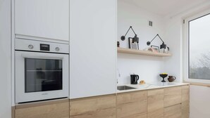 A modern kitchen with a built-in oven, wooden cabinets, and a window providing natural light.