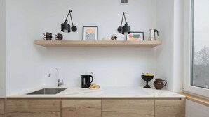 A kitchen with wooden cabinets, a white countertop, a sink, and two shelves with various items.
